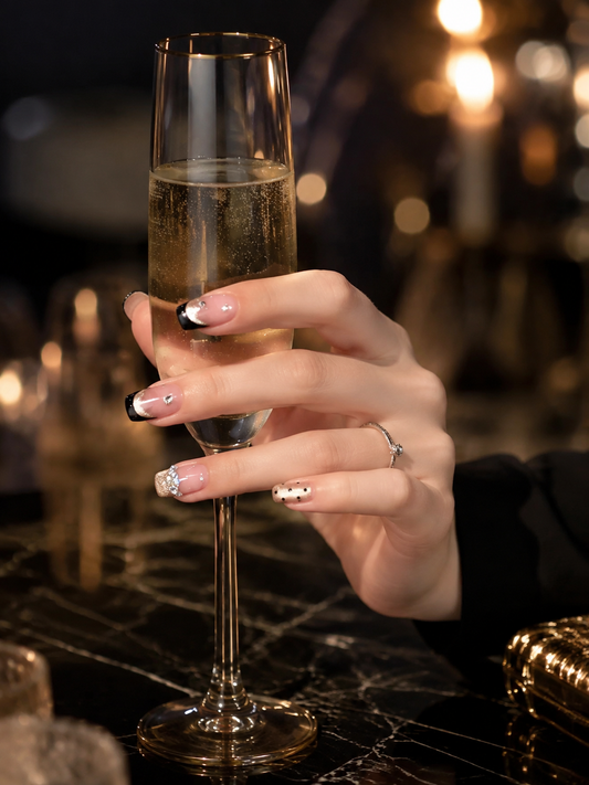 Midnight Spark black French and champagne glitter press-on nails styled with a champagne glass for an evening look
